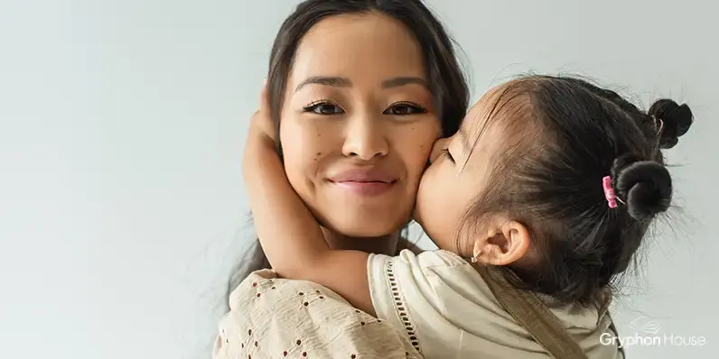 Woman holding a baby who is hugging her neck and kissing her on the cheek