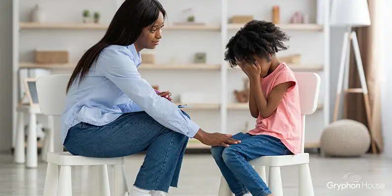 Adult speaking to a young child who is holding their head in their hands