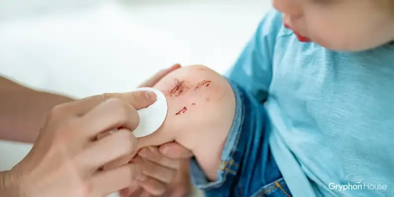 Adult using a medical wipe to clean a scrape of the knee of a young child