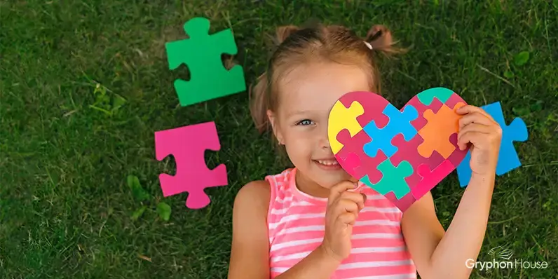 Young girl lying on the ground with colorful puzzle pieces lying around her, holding a heart made from colorful puzzle pieces