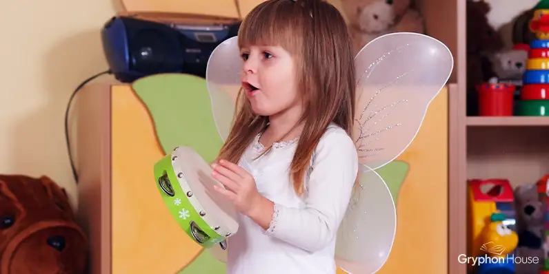 Small girl wearing a fairy outfit playing a tambourine in a childcare setting